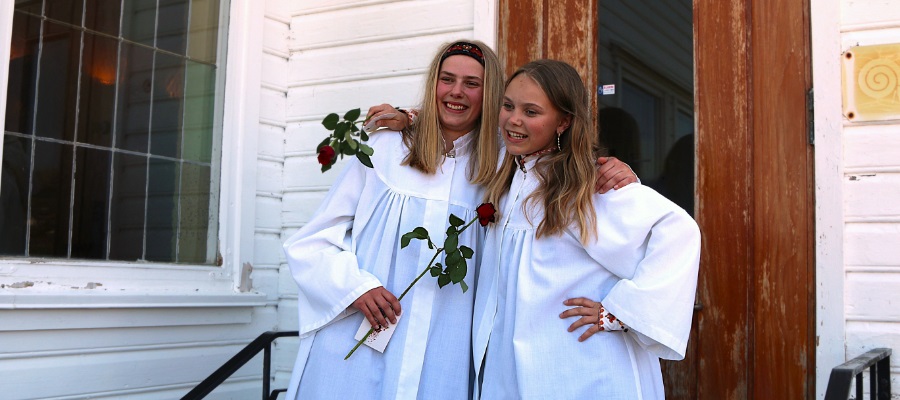 Konfirmanter i hvite kapper står i kø for å få komme inn i kirken. Foto.